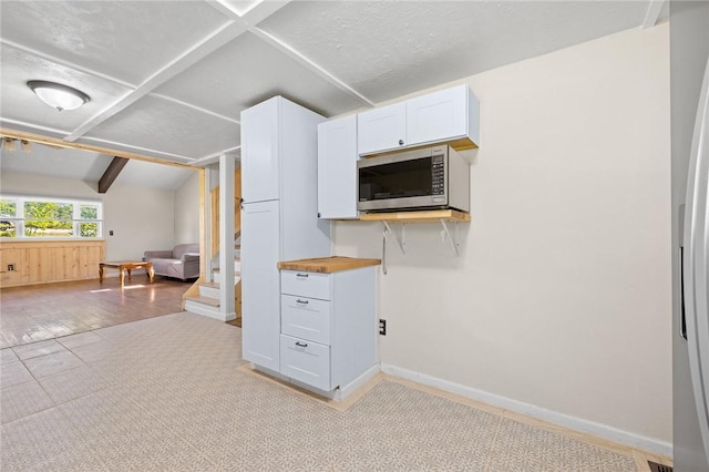 kitchen with baseboards, stainless steel microwave, white cabinetry, open floor plan, and vaulted ceiling