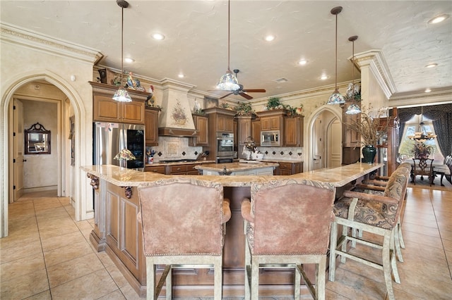 kitchen with arched walkways, a large island with sink, light tile patterned floors, and appliances with stainless steel finishes