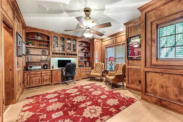 home office with a ceiling fan, a textured ceiling, built in features, built in desk, and light wood-type flooring