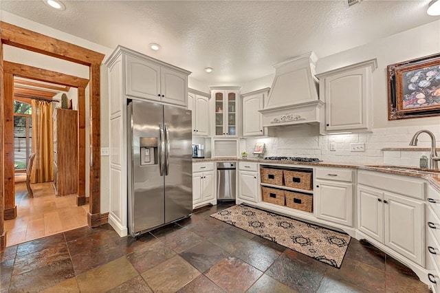kitchen featuring a sink, stone tile flooring, light stone countertops, appliances with stainless steel finishes, and custom exhaust hood