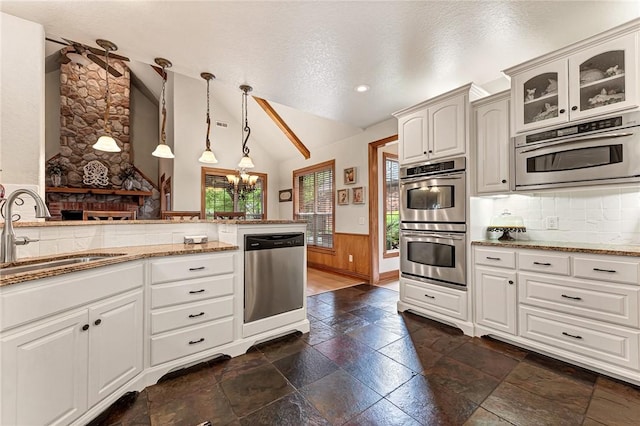 kitchen featuring a sink, lofted ceiling, stone tile flooring, glass insert cabinets, and appliances with stainless steel finishes