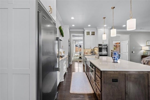 kitchen with stainless steel appliances, ornamental molding, a sink, light countertops, and white cabinets