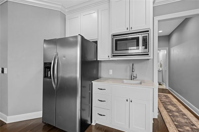 kitchen featuring appliances with stainless steel finishes, a sink, dark wood-style flooring, white cabinetry, and crown molding