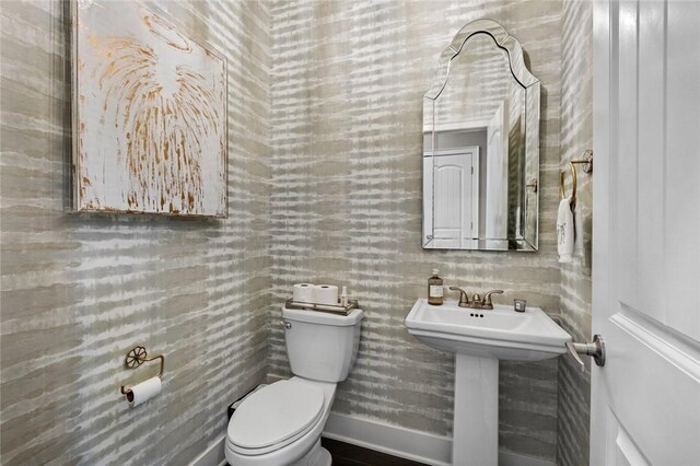 half bath with toilet, a sink, and baseboards
