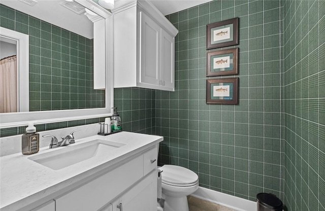 bathroom with toilet, vanity, and tile walls