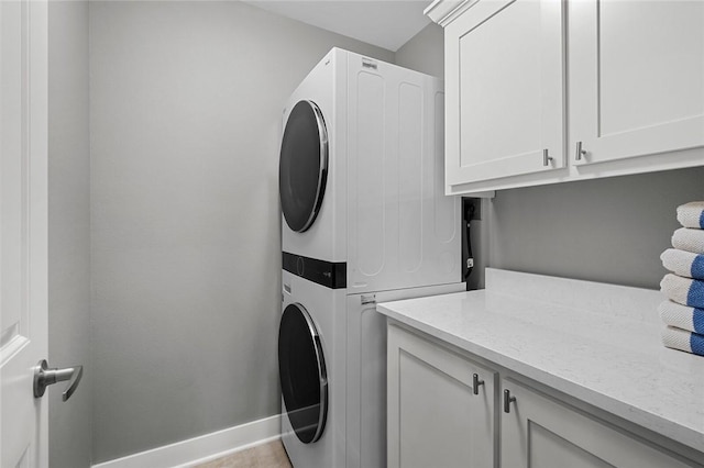 laundry area with stacked washer and clothes dryer, cabinet space, and baseboards