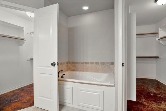full bathroom with a walk in closet, finished concrete floors, a garden tub, recessed lighting, and baseboards