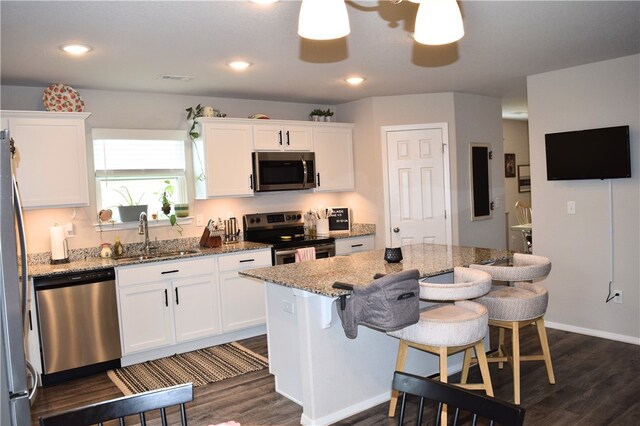 kitchen with stainless steel appliances, a sink, dark wood-type flooring, white cabinetry, and a breakfast bar