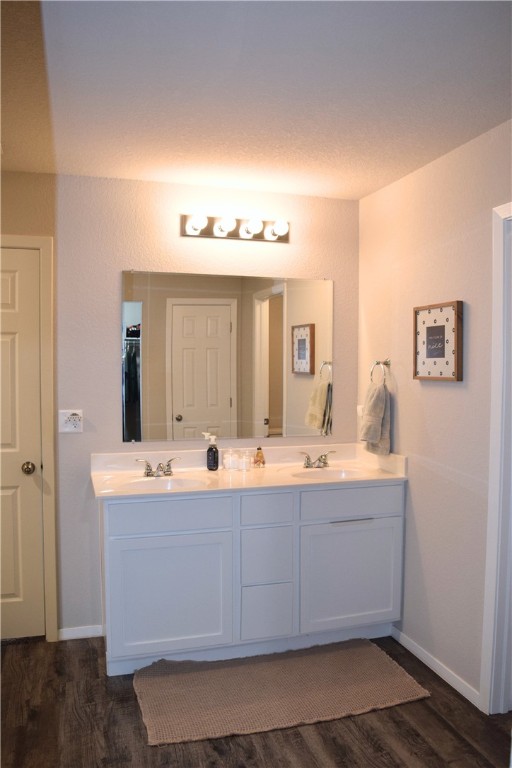 full bath featuring wood finished floors, double vanity, and baseboards