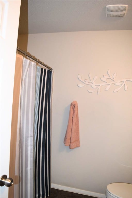 bathroom with toilet, baseboards, and a shower with curtain