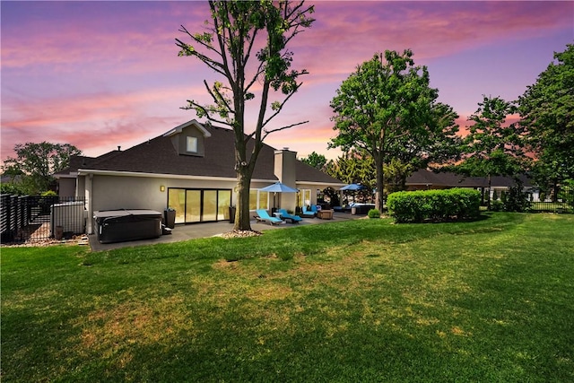 back of house at dusk featuring a hot tub, a patio area, and roof with shingles