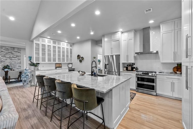 kitchen featuring stainless steel appliances, wall chimney exhaust hood, a sink, recessed lighting, and light wood-style floors