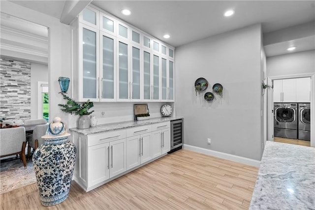 kitchen with beverage cooler, washer and dryer, light stone countertops, baseboards, and white cabinetry