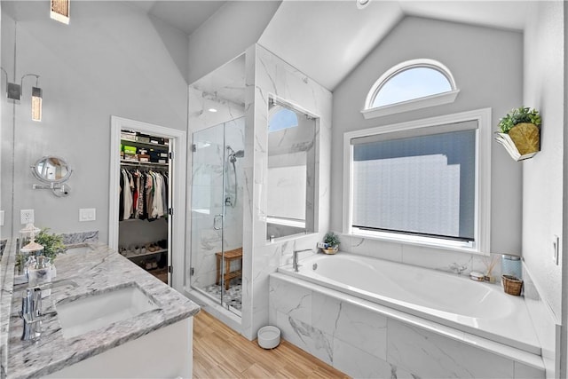 bathroom featuring a marble finish shower, a garden tub, lofted ceiling, a spacious closet, and wood finished floors