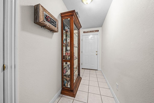 hallway with light tile patterned floors, baseboards, and a textured wall