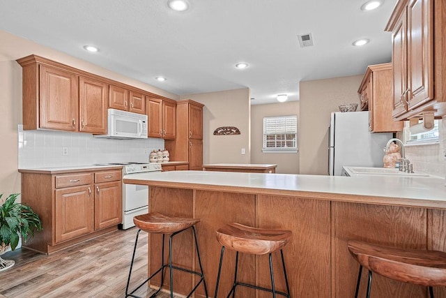kitchen featuring white appliances, a peninsula, light wood-type flooring, backsplash, and a sink