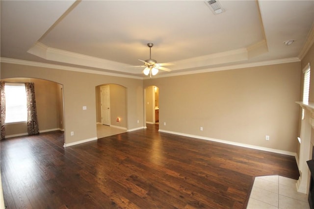 unfurnished living room featuring a tray ceiling, arched walkways, healthy amount of natural light, hardwood / wood-style floors, and ornamental molding