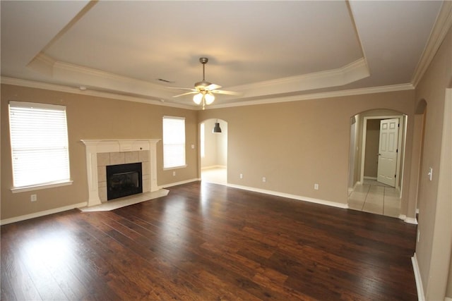 unfurnished living room with a raised ceiling, arched walkways, a ceiling fan, dark wood finished floors, and crown molding