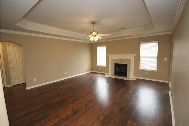 unfurnished living room featuring a raised ceiling, dark wood finished floors, a ceiling fan, arched walkways, and baseboards