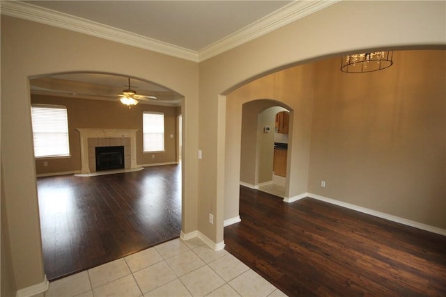 unfurnished living room with ornamental molding, ceiling fan, wood finished floors, arched walkways, and a fireplace