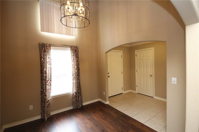 foyer featuring arched walkways, a chandelier, wood-type flooring, baseboards, and high vaulted ceiling