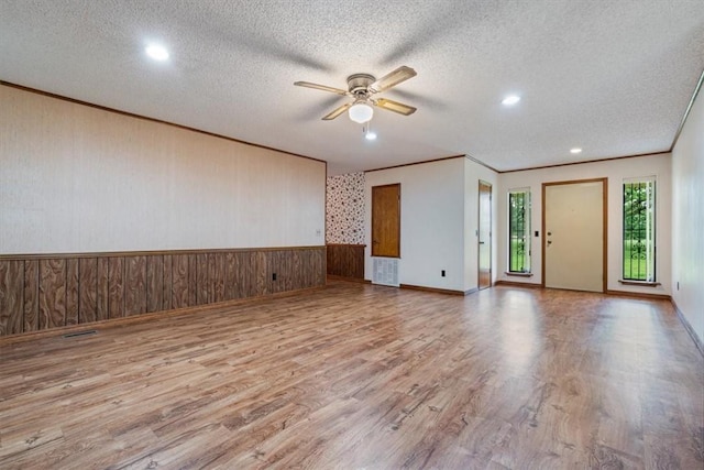 unfurnished room with wood finished floors, a ceiling fan, a textured ceiling, wooden walls, and ornamental molding