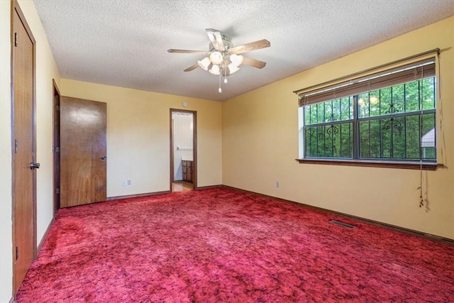 unfurnished bedroom featuring carpet, a textured ceiling, baseboards, ensuite bath, and ceiling fan