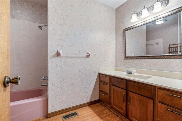 full bath with wood finished floors, wallpapered walls, vanity, and shower / tub combination