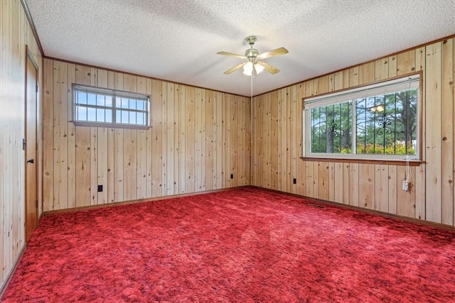 unfurnished room with plenty of natural light, a textured ceiling, a ceiling fan, wooden walls, and carpet