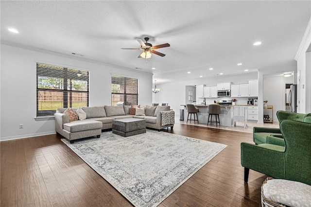 living area featuring a ceiling fan, recessed lighting, baseboards, dark wood-type flooring, and ornamental molding