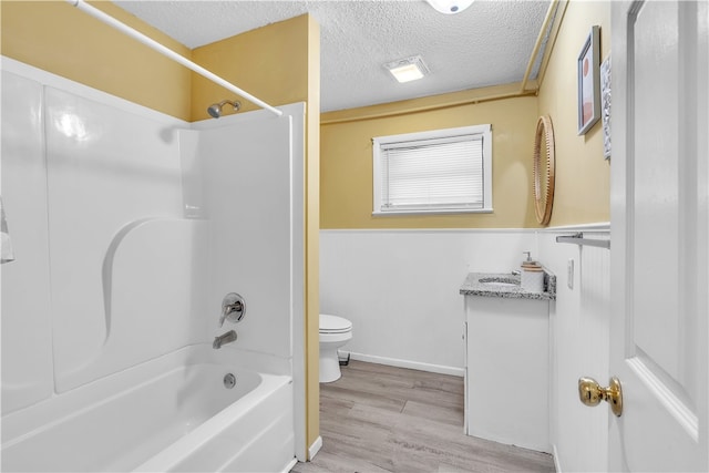 full bath featuring toilet, bathtub / shower combination, wood finished floors, vanity, and wainscoting