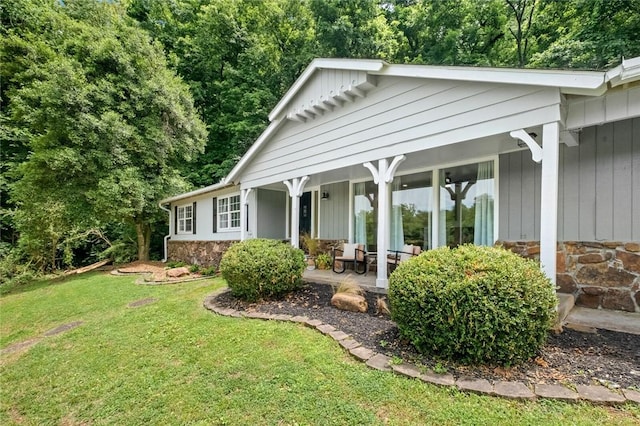 back of house with stone siding, a yard, covered porch, and board and batten siding