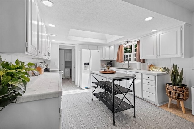 kitchen featuring white appliances, a sink, tile counters, white cabinetry, and recessed lighting