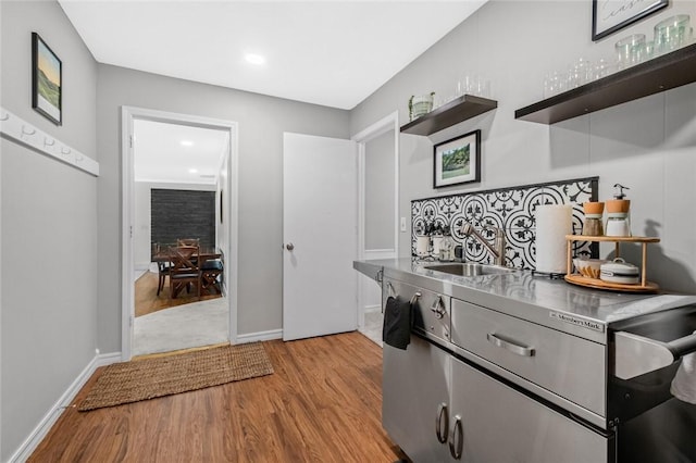 kitchen featuring stainless steel countertops, open shelves, light wood-style floors, a sink, and baseboards