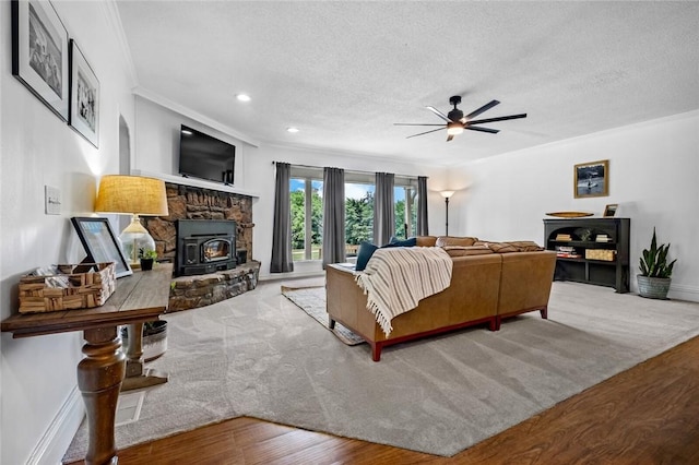 living area featuring a wood stove, wood finished floors, ceiling fan, a textured ceiling, and crown molding