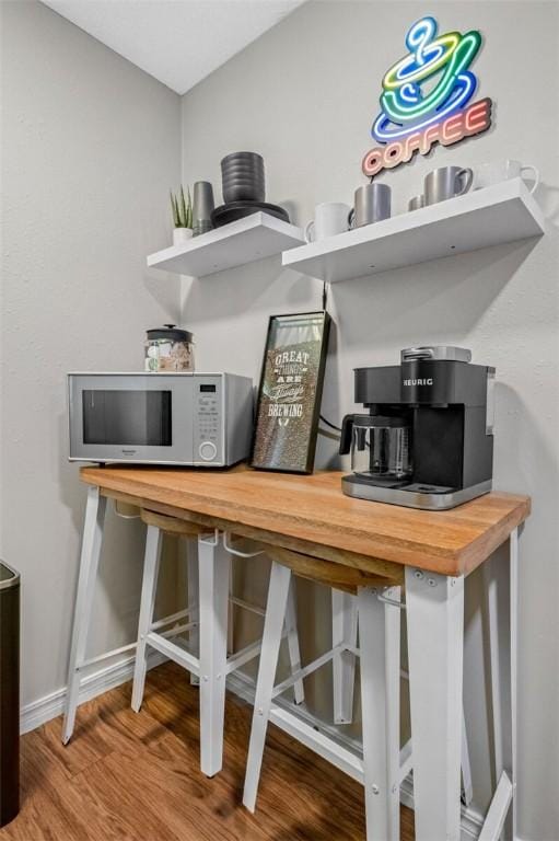 bar featuring white microwave, wood finished floors, and baseboards