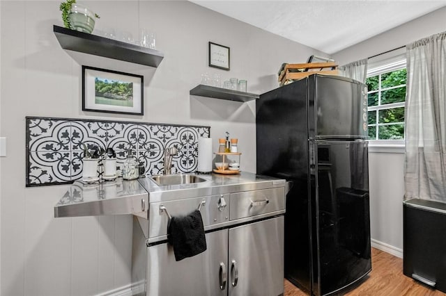 kitchen featuring freestanding refrigerator, a sink, open shelves, light wood-style floors, and baseboards