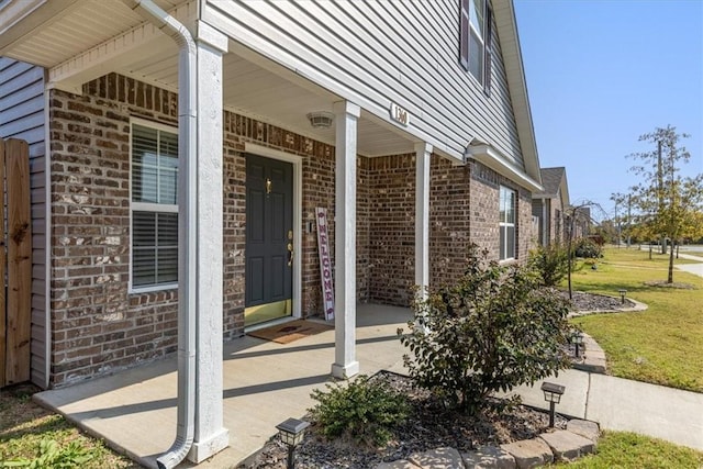 view of exterior entry with brick siding, a porch, and a yard