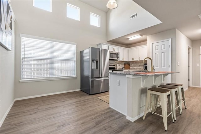 kitchen with appliances with stainless steel finishes, white cabinets, light wood-style flooring, a kitchen breakfast bar, and a high ceiling