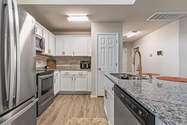 kitchen with appliances with stainless steel finishes, a sink, light wood finished floors, white cabinets, and light stone counters