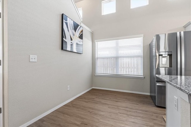 kitchen with stainless steel fridge with ice dispenser, light wood-style flooring, baseboards, and stone countertops