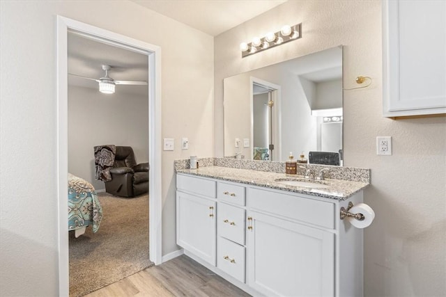 ensuite bathroom with wood finished floors, double vanity, ceiling fan, and baseboards