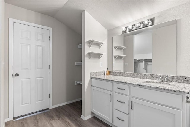 bathroom featuring wood finished floors, vanity, lofted ceiling, and baseboards