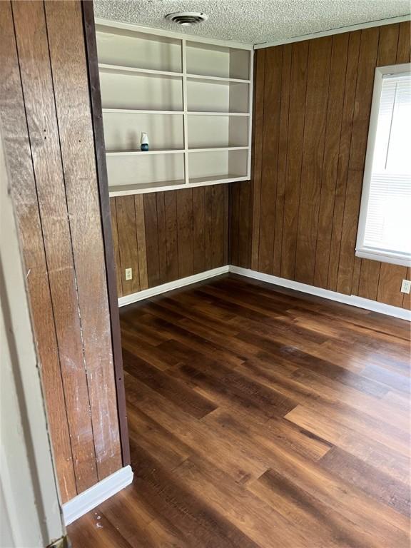 spare room featuring a textured ceiling, wood finished floors, wood walls, and baseboards