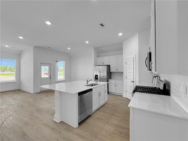 kitchen with stainless steel appliances, a sink, light wood-style flooring, decorative backsplash, and an island with sink
