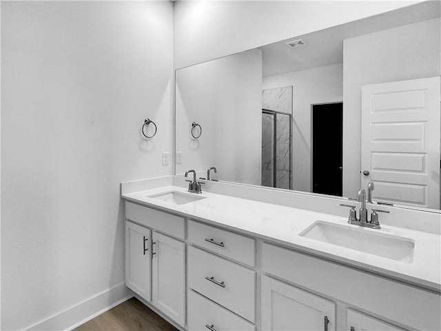 full bath featuring a marble finish shower, double vanity, baseboards, and wood finished floors