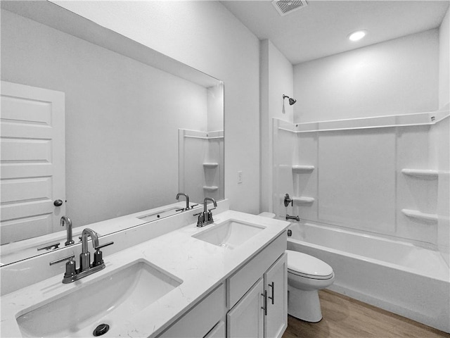 bathroom featuring wood finished floors, toilet, double vanity, shower / bathtub combination, and recessed lighting