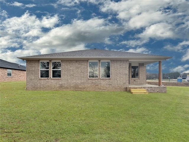 rear view of house with brick siding, a lawn, and roof with shingles