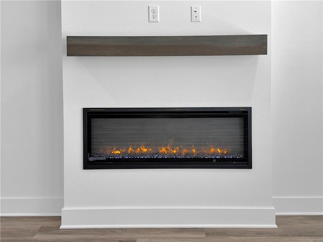detailed view of a glass covered fireplace, wood finished floors, and baseboards