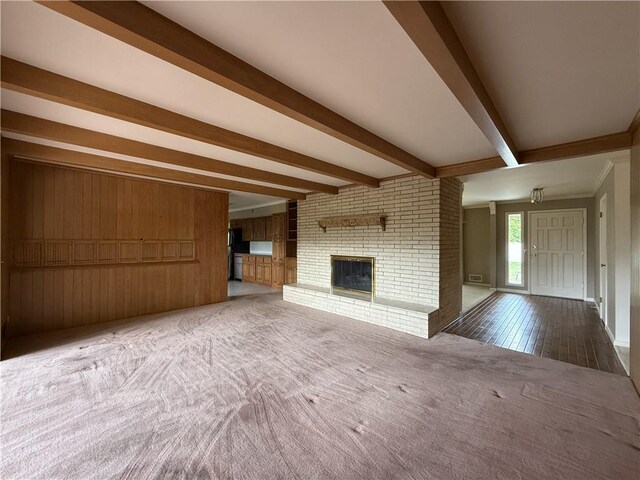 unfurnished living room featuring beam ceiling, carpet floors, a brick fireplace, and wooden walls